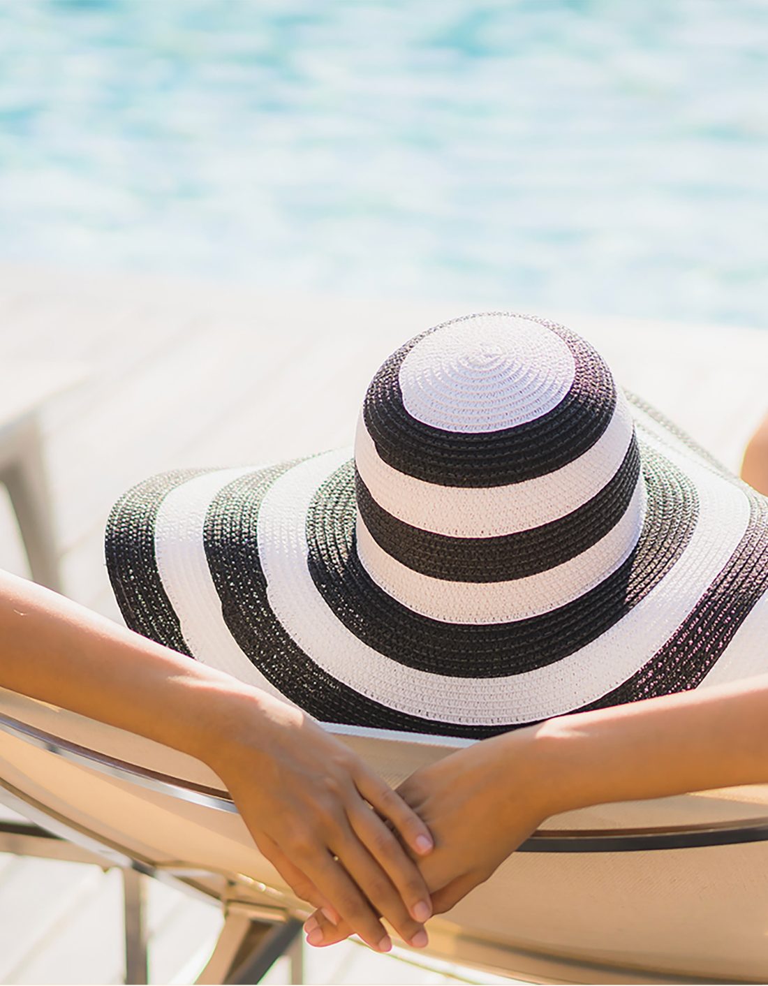 A person relaxing poolside in a black-and-white striped sun hat