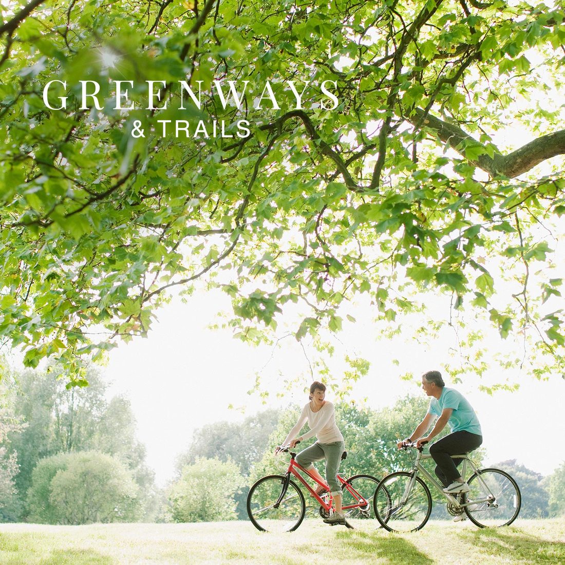 Two cyclists riding beneath a leafy tree canopy, with the title Greenways and Trails